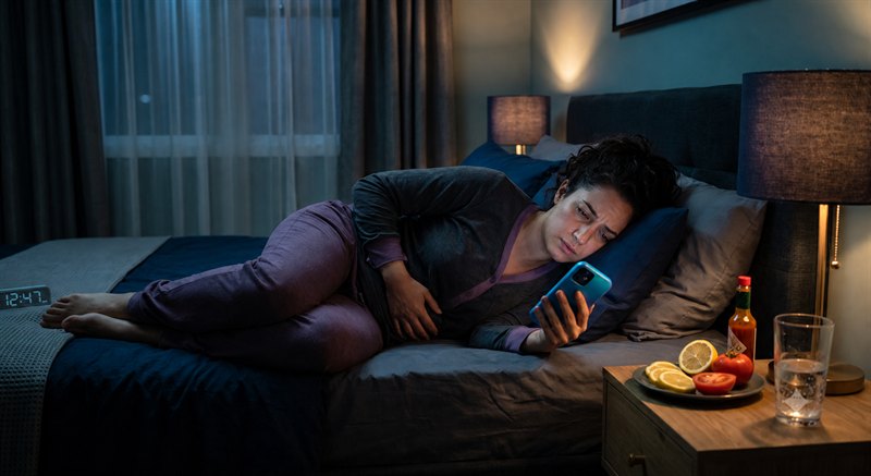 Adult lying down with a phone and tomato, citrus and sauce on a bedside table